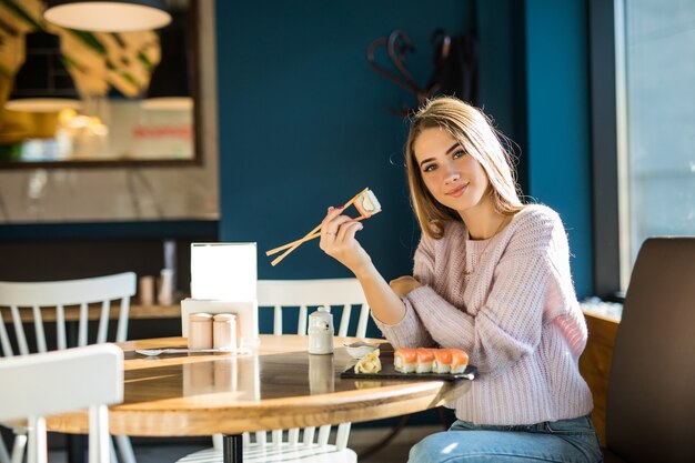 Giovane ragazza in maglione bianco che mangia sushi per pranzo in un piccolo caffe