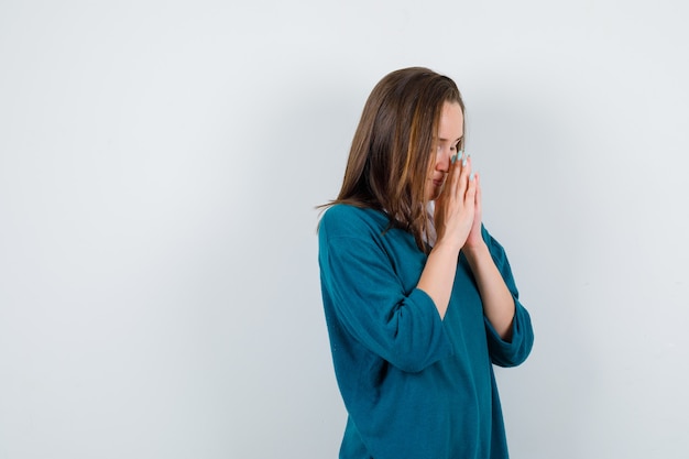 Giovane ragazza in maglione con scollo a V, camicia che mostra il gesto di namaste, in piedi di lato e sembra grata.