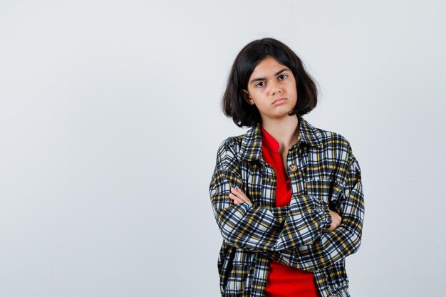 Giovane ragazza in piedi con le braccia incrociate in camicia a quadri e t-shirt rossa e sembra seria. vista frontale.