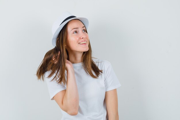 Giovane ragazza in posa mentre cerca in t-shirt bianca, cappello e sembra bellissima, vista frontale.