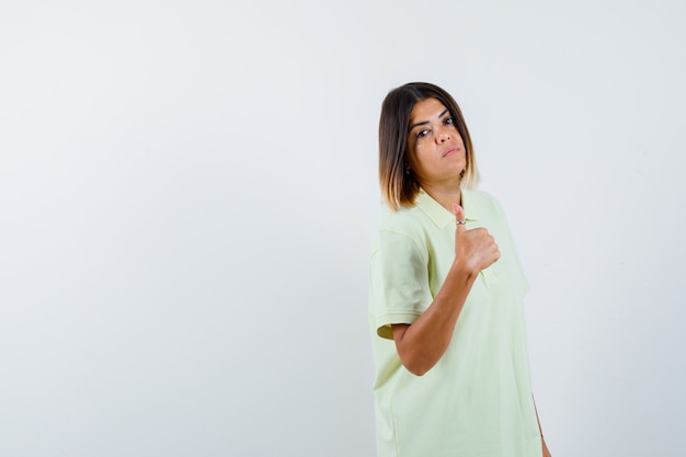 Giovane ragazza in t-shirt che mostra il pollice in alto e guardando fiducioso, vista frontale.