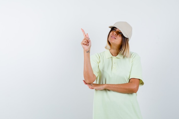 Giovane ragazza in t-shirt e berretto alzando il dito indice nel gesto di eureka e guardando sensibile, vista frontale.