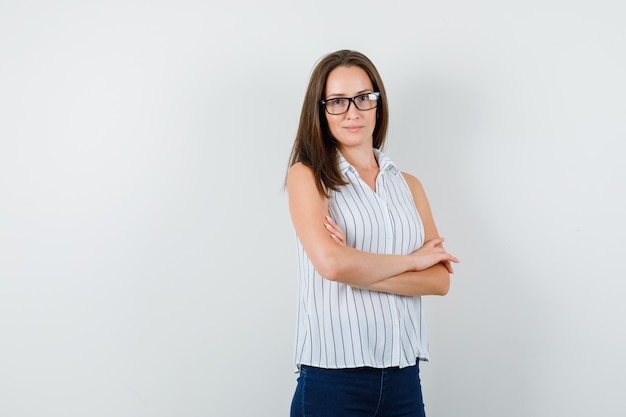 Giovane ragazza in t-shirt, jeans in piedi con le braccia incrociate e guardando fiducioso, vista frontale.