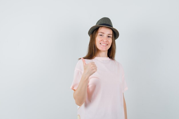 Giovane ragazza in t-shirt rosa, cappello che mostra il pollice in alto e sembra allegra, vista frontale.