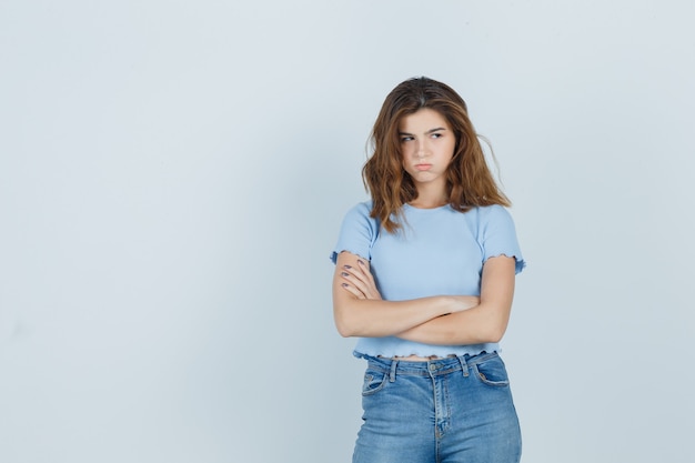 Giovane ragazza incrociando le braccia in t-shirt, jeans e guardando offeso, vista frontale.