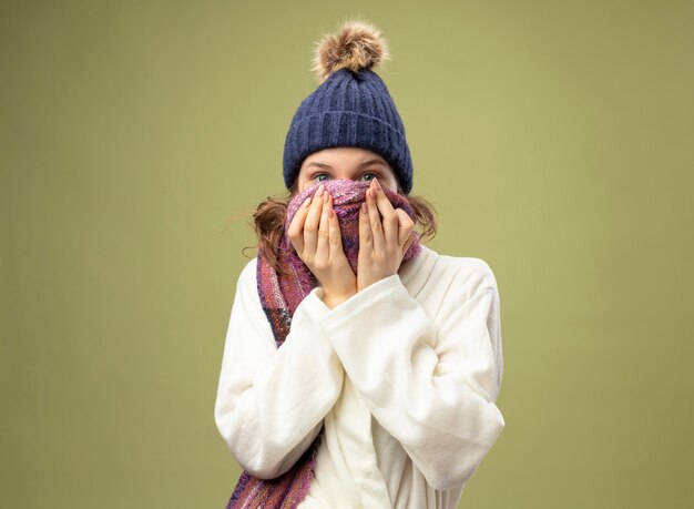 Giovane ragazza malata indossa veste bianca e cappello invernale con sciarpa viso coperto con sciarpa