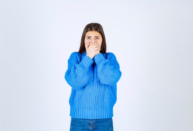 giovane ragazza modello in maglione blu coning bocca con una mano su bianco-grigio.
