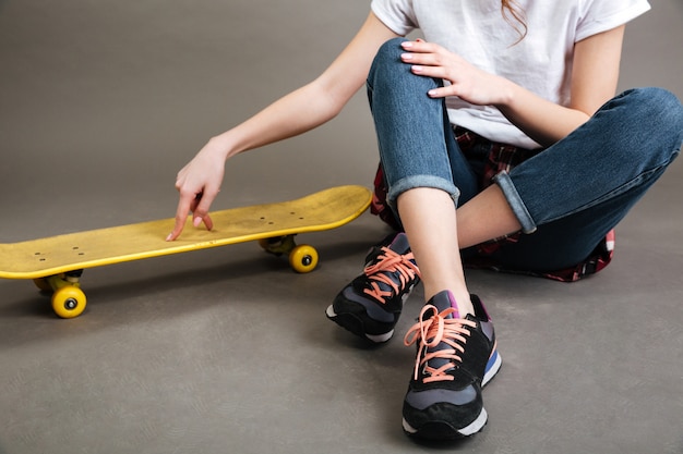 Giovane ragazza seduta sul pavimento con skateboard