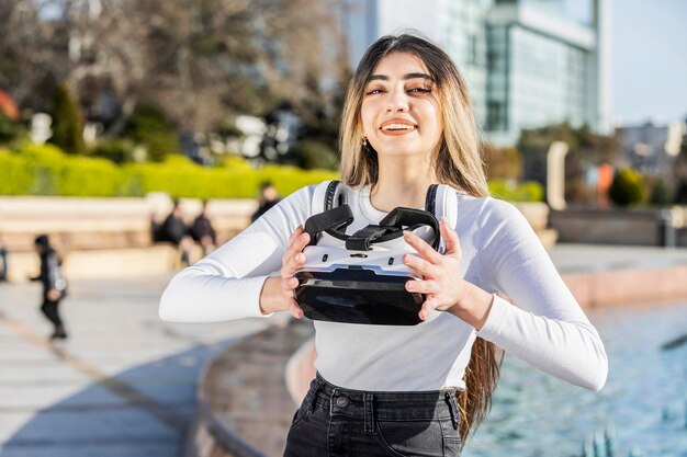 Giovane ragazza sorridente che cerca di indossare la realtà virtuale per strada Foto di alta qualità