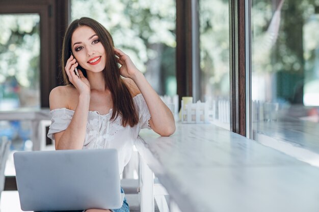 Giovane ragazza sorridente, parlando al telefono con un computer portatile sulle gambe