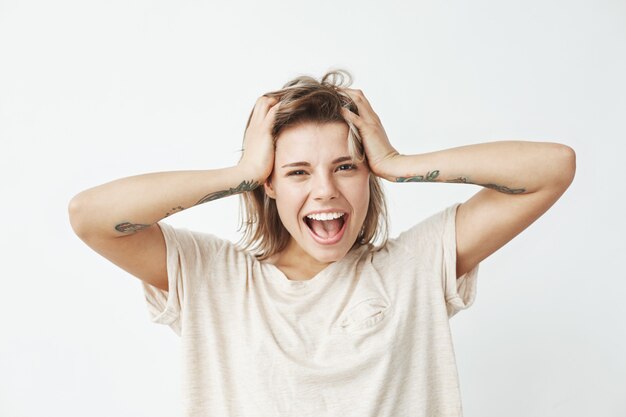 Giovane ragazza tatuata allegra emozionale che sorride con i capelli commoventi della bocca aperta.