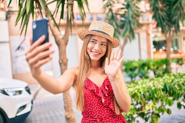 Giovane ragazza turistica caucasica che sorride felice facendo videochiamata utilizzando lo smartphone in città.