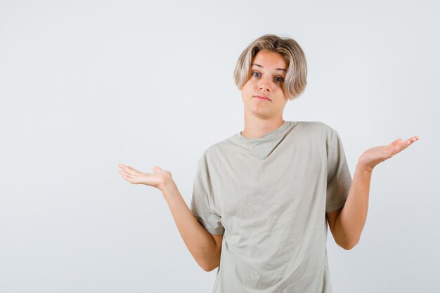 Giovane ragazzo adolescente che mostra gesto impotente in maglietta e sembra confuso, vista frontale.