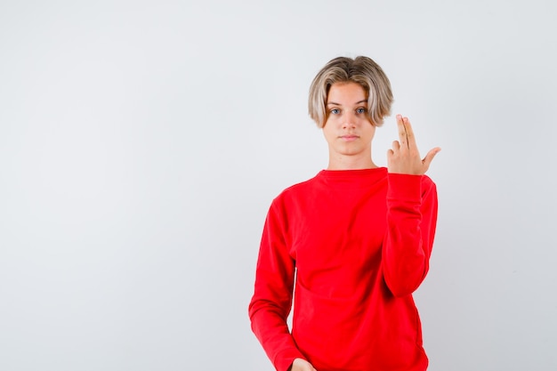 Giovane ragazzo adolescente che mostra il gesto della pistola in maglione rosso e sembra serio, vista frontale.