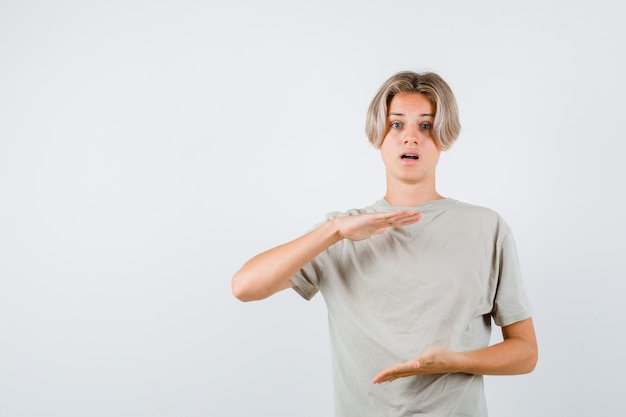 Giovane ragazzo adolescente che mostra segno di grandi dimensioni in t-shirt e sembra perplesso. vista frontale.