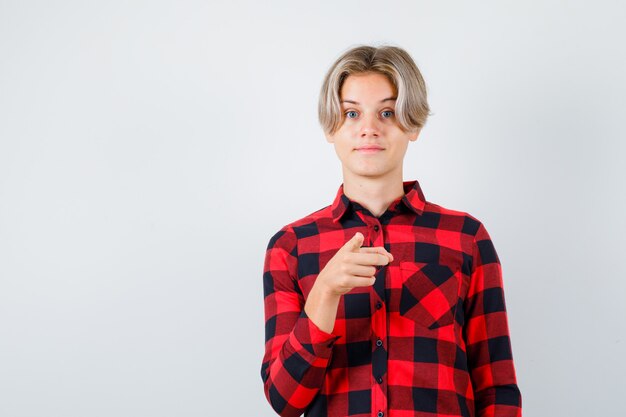 Giovane ragazzo adolescente in camicia a quadri che punta davanti e sembra allegro, vista frontale.