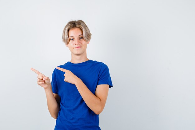 Giovane ragazzo adolescente in maglietta blu che punta a sinistra e sembra allegro, vista frontale.