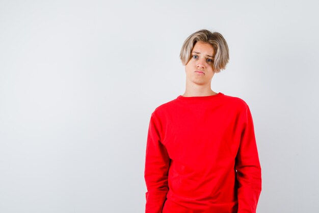 Giovane ragazzo adolescente in maglione rosso e guardando deluso, vista frontale.