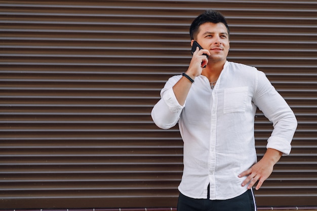 Giovane ragazzo alla moda in camicia parlando al telefono sulla superficie semplice