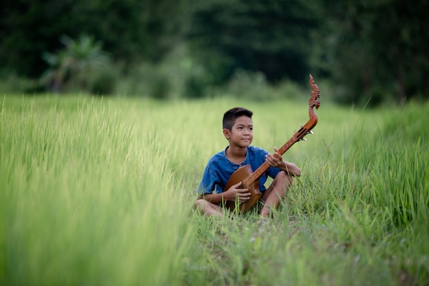 Giovane ragazzo asiatico con la chitarra fatta a mano all'aperto, paese di vita