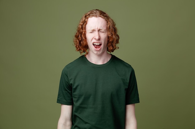 Giovane ragazzo bello arrabbiato che indossa una maglietta verde isolata su sfondo verde