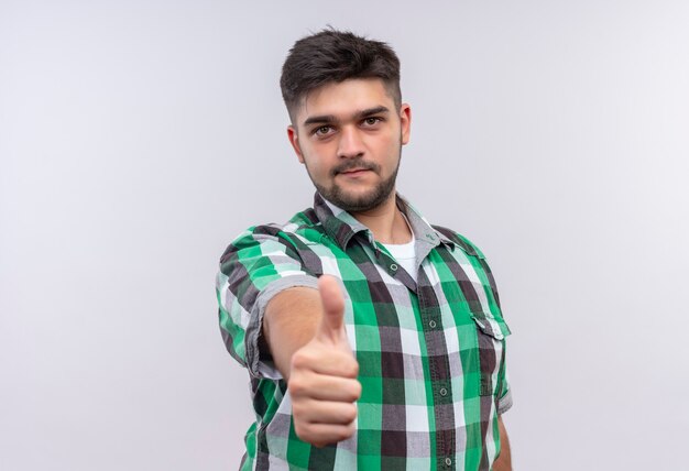 Giovane ragazzo bello che indossa la camicia a scacchi facendo come segno in piedi sul muro bianco