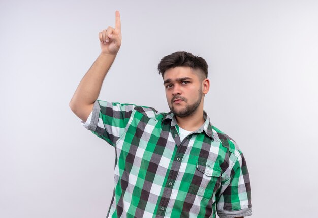 Giovane ragazzo bello che indossa la camicia a scacchi guardando rivolto verso l'alto con l'indice in piedi sopra il muro bianco