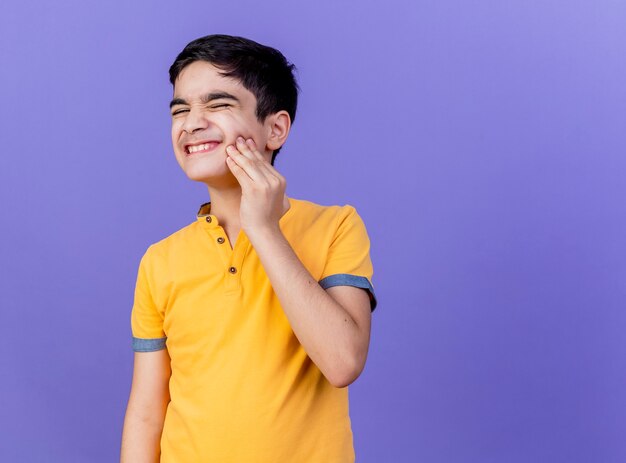 Giovane ragazzo caucasico dolorante che tocca la guancia che ha mal di denti isolato sulla parete viola con lo spazio della copia