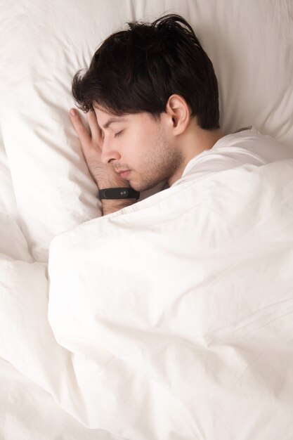 Giovane ragazzo che dorme nel letto indossando orologio intelligente, inseguitore del sonno