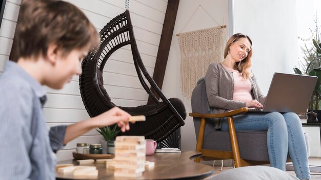 Giovane ragazzo che gioca jenga mentre la mamma sta lavorando