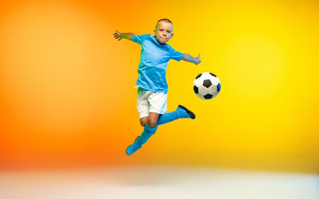 Giovane ragazzo come giocatore di calcio in abbigliamento sportivo che si esercita sul giallo sfumato al neon