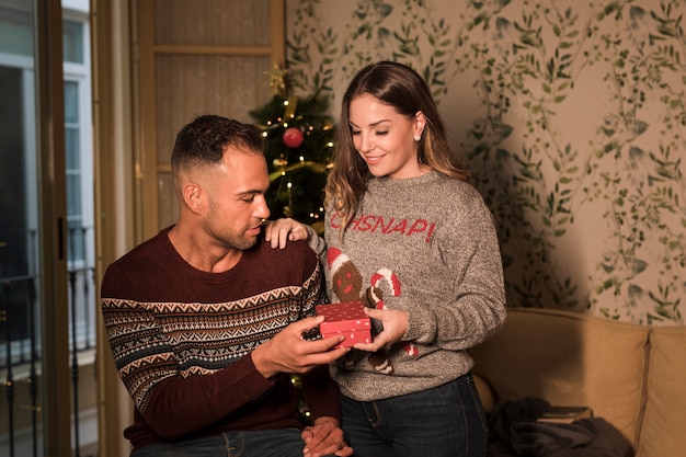 Giovane ragazzo con scatola regalo e signora allegra sul divano vicino all&#39;albero di Natale