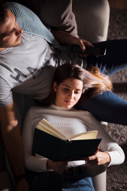 Giovane ragazzo con telecomando TV e signora con il libro sul divano