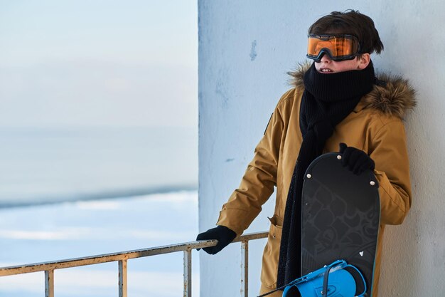 Giovane ragazzo in giacca calda si sta godendo le vacanze invernali con il suo snowboard.