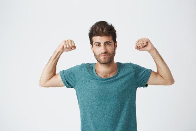 Giovane ragazzo ispanico sportivo in maglietta blu e acconciatura alla moda, che mostra il gioco con i muscoli in posa per il servizio fotografico della rivista sportiva.