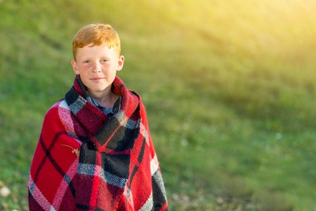 Giovane ragazzo sveglio con la coperta che esamina macchina fotografica