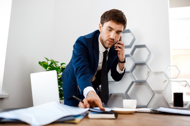 Giovane riuscito uomo d'affari che parla sul telefono, fondo dell'ufficio.