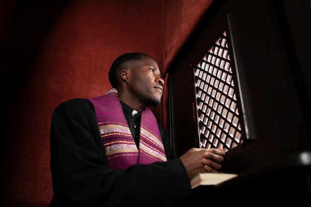 Giovane sacerdote maschio all'interno del confessionale in chiesa