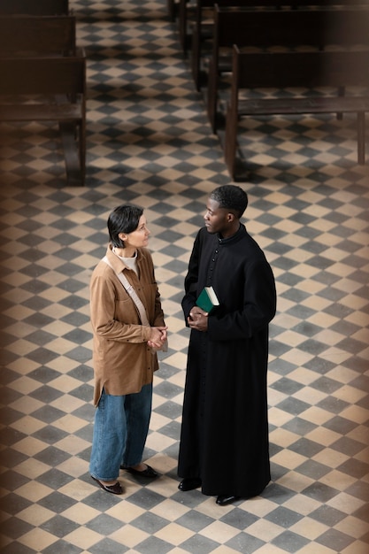 Giovane sacerdote maschio e donna che parlano nella chiesa mentre tengono una bibbia