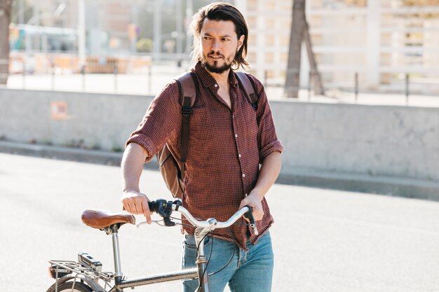 Giovane serio con il suo zaino a piedi con la bicicletta