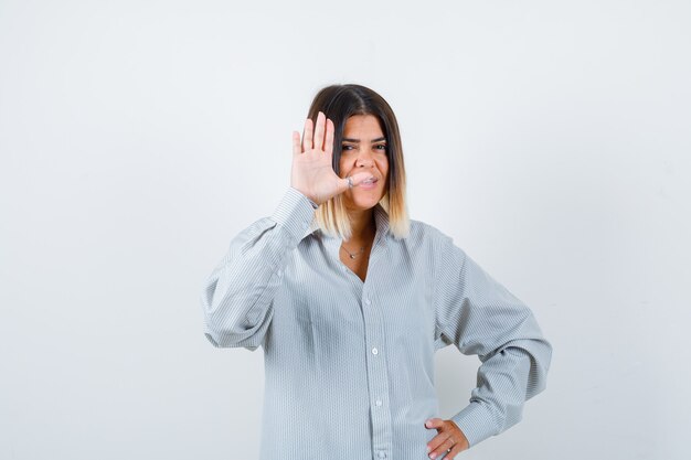 Giovane signora agitando la mano per salutare in camicia oversize e guardando felice vista frontale.