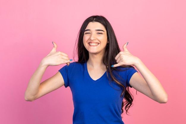 Giovane signora allegra alzò le mani e sorridente su sfondo rosa