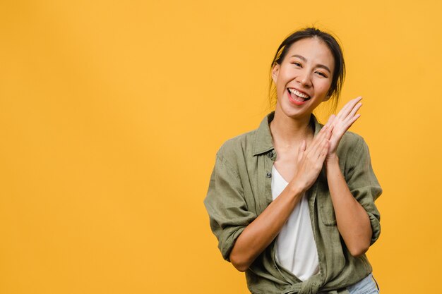 Giovane signora asiatica con un'espressione positiva, sorride ampiamente, vestita con abiti casual sul muro giallo. La donna felice adorabile felice si rallegra del successo. Concetto di espressione facciale.