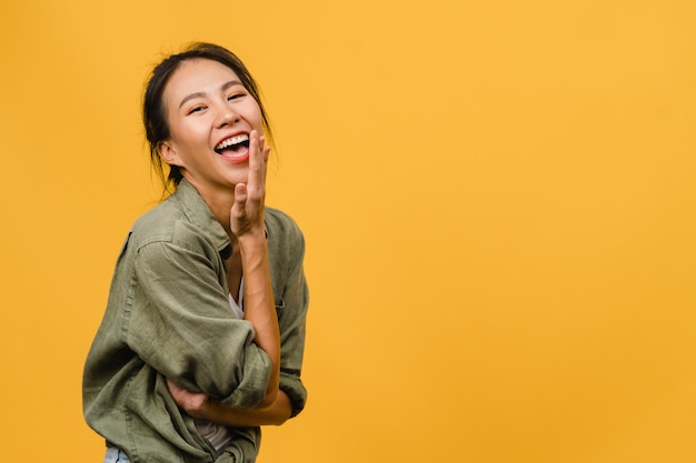 Giovane signora asiatica con un'espressione positiva, sorride ampiamente, vestita con abiti casual sul muro giallo. La donna felice adorabile felice si rallegra del successo. Concetto di espressione facciale.