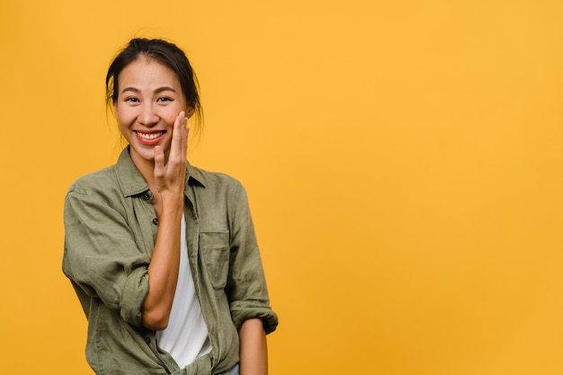 Giovane signora asiatica con un'espressione positiva, sorride ampiamente, vestita con abiti casual sul muro giallo. La donna felice adorabile felice si rallegra del successo. Concetto di espressione facciale.