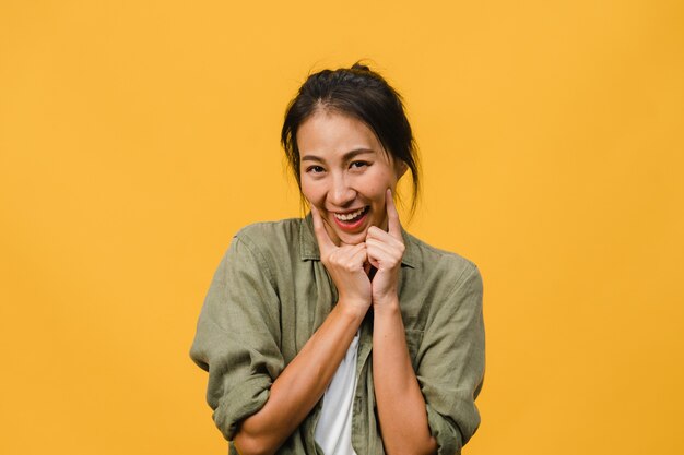 Giovane signora asiatica con un'espressione positiva, sorride ampiamente, vestita con abiti casual sul muro giallo. La donna felice adorabile felice si rallegra del successo. Concetto di espressione facciale.