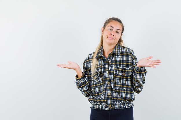 Giovane signora che mostra gesto impotente in camicia, pantaloncini e sguardo confuso, vista frontale.