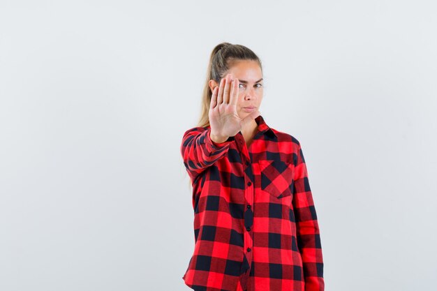 Giovane signora che mostra il gesto di arresto in camicia casual e sembra seria. vista frontale.