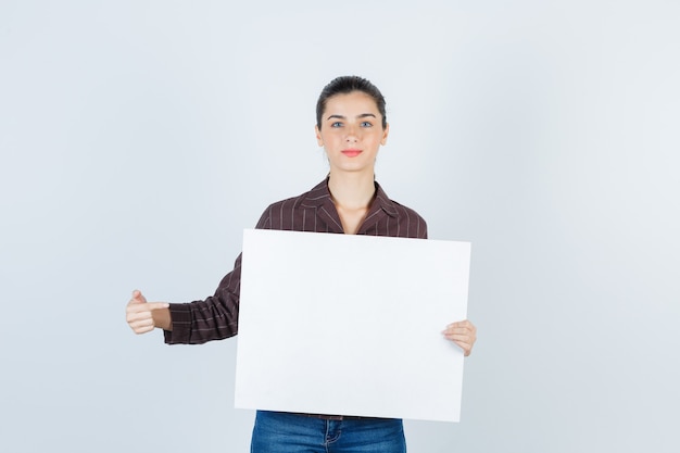 Giovane signora che mostra poster di carta in camicia, vista frontale dei jeans.