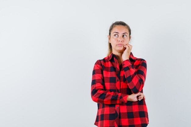 Giovane signora che osserva in su in camicia controllata e che sembra pensieroso